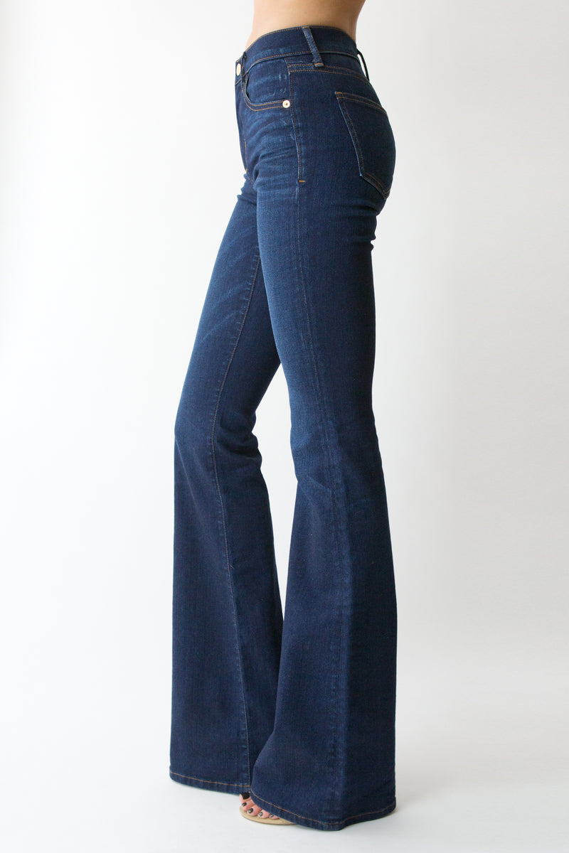 Side View of Midheaven’s Mid-Rise Indigo Flare  ITEM RUNS SMALL, CONSIDER SIZING UP   Details: Model is 6' and is wearing 4" heels. Rise: 9” Inseam: 38” Leg Opening: 21” Fabric contents: 98% Cotton - 2% Elastane